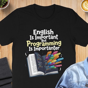 May include: A black short-sleeve t-shirt featuring the white and yellow text "English Is Important But Programming Is Importanter" above an open book graphic with colorful code snippets emerging from the pages in various rectangular blocks.