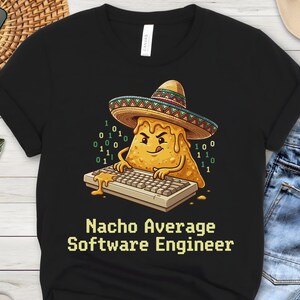 May include: A black t-shirt featuring a graphic of a cartoon nacho chip wearing a colorful sombrero, typing on a computer keyboard with green binary code floating nearby. The text below the graphic reads, "Nacho Average Software Engineer."