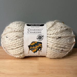 May include: A skein of white yarn with brown flecks, labeled "CHARISMA® CHARISME" and "Loops & Threads". The label also includes the yarn weight, yardage, and a pattern for a blanket.