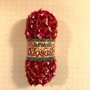 May include: A skein of Patons Mosaic yarn in a red, pink, and orange colorway. The yarn is a bulky weight and has a fuzzy texture.