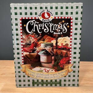 May include: A Christmas cookbook, "Gooseberry Patch Christmas Book 3," features a festive cover with a green and white plaid pattern. The cover displays the title, images of holiday gifts, and text that reads "Delicious old-fashioned recipes, handmade holiday gifts & ideas for frosty fun!"