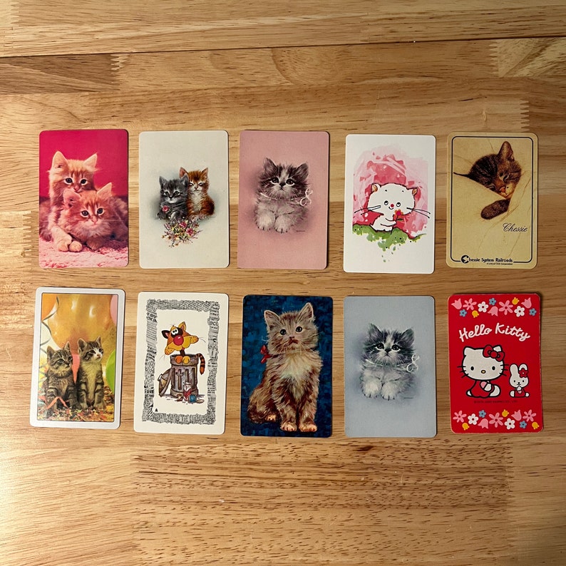 K&ouml;nnte beinhalten: Ein Set aus zehn Vintage-Sammelkarten mit verschiedenen Illustrationen von Katzen. Die Karten sind auf wei&szlig;em Hintergrund mit bunten Bildern von Katzen in verschiedenen Posen und Umgebungen gedruckt. Die Karten enthalten Text wie "Hello Kitty" und "Cherrie".