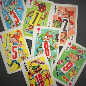 May include: A set of ten playing cards featuring different illustrations and numbers. The cards are arranged in a semi-circle on a gray surface. The numbers on the cards are 1, 2, 3, 5, 8, 9, and 10.