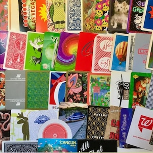 May include: A collection of colorful playing cards with various designs, including a unicorn, a hot air balloon, a plane, a flamingo, and a cityscape. The cards feature text such as "To Fabulous Las Vegas", "United Airlines", "Cancun", and "All That".