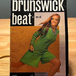 May include: A vintage magazine cover with the title "Brunswick Beat" in large white letters on a black background. The cover features a woman in a green sweater and shorts. The text "s 'em all" is also visible.