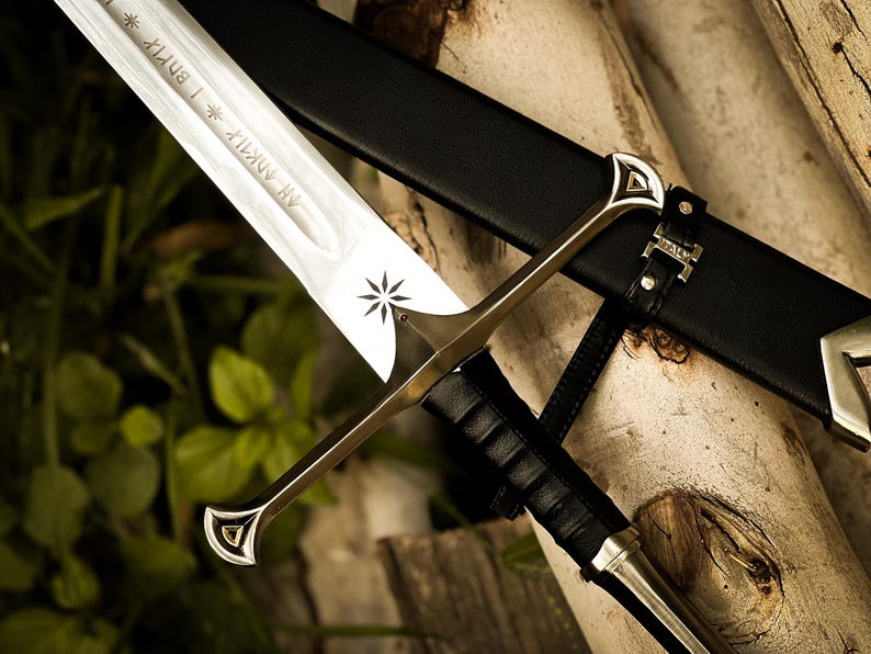 Puede incluir: Espada plateada y dorada con una vaina de cuero negro. La hoja de la espada tiene texto grabado y un dise&ntilde;o de estrella. La empu&ntilde;adura es dorada con detalles plateados. La vaina es negra con herrajes plateados.