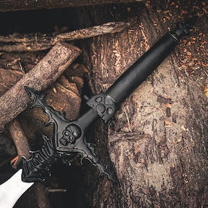 May include: A black fantasy sword with a skull design on the hilt and a white blade. The sword is set against a backdrop of wood logs and yellow foliage, creating a dramatic contrast.