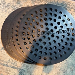 May include: A set of four circular black plastic discs featuring a grid of evenly spaced circular perforations. Each disc is embossed with the text Gulf Coast Grabs and the number 1. The discs are stacked in a slightly offset, overlapping arrangement.
