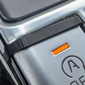 May include: Close-up of a car's start/stop button. The button is silver with an orange indicator light and the symbol of a circle with an "A" and an arrow. The word "OFF" is below the symbol.