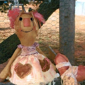 Könnte beinhalten: Eine handgemachte Stoffpuppe mit rosa Haaren und einem rosa-braunen Kleid. Die Puppe hält ein herzförmiges Kissen mit einem Etikett, auf dem steht "Du bist mein Valentinstag - öffne in der Nähe eines Fensters".