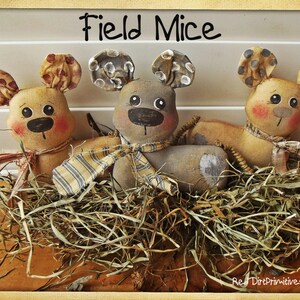 May include: Three handmade fabric field mice in a nest of straw. The mice are brown and tan with black eyes and pink cheeks. The middle mouse is gray with white polka dots on its ears. The text "Field Mice" is written above the mice.
