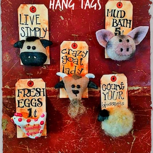 Op de afbeelding: Een verzameling van vijf handgemaakte vilten boerderijdier-hanglabels met beschilderde houten borden. De borden bevatten zinnen als "Eenvoudig leven", "Crazy Goat Lady", "Verse eieren 1c", "Modderbad 5c" en "Tel je zegeningen".