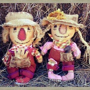 May include: Two handmade rag dolls dressed as scarecrows. The dolls are wearing straw hats, plaid shirts, and overalls. They are sitting in a pile of hay.