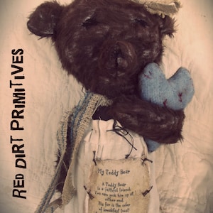 Puede incluir: Un oso de peluche marrón con un corazón azul en sus patas, sentado sobre un fondo de tela blanca. El oso está hecho de un saco de pienso y tiene una etiqueta que dice "Mi oso de peluche es un amigo fiel. Puedes cogerlo por cualquier extremo. Su pelaje es del color de las tostadas del desayuno. Y siempre está ahí cuando lo necesitas."