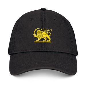 Puede incluir: Gorra de béisbol negra con un emblema amarillo bordado de un león sosteniendo una espada frente a un sol naciente. La gorra tiene una visera curva y un botón en la parte superior. El emblema está en la parte delantera.