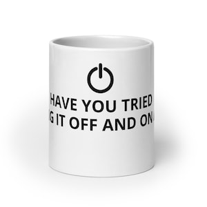 May include: White ceramic coffee mug with a black power button icon and the text "HAVE YOU TRIED TURNING IT OFF AND ON". The mug is cylindrical and has a handle.