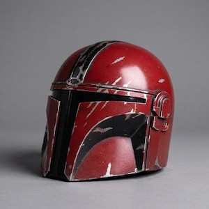 Puede incluir: Un casco rojo y negro con detalles plateados. El casco tiene un acabado brillante y un aspecto desgastado, con ara&ntilde;azos y marcas de desgaste. El dise&ntilde;o incluye una visera negra y una franja central. El casco es probablemente un accesorio o art&iacute;culo de colecci&oacute;n.