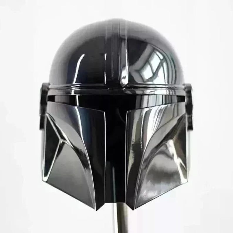May include: A glossy black Mandalorian helmet with a sleek, futuristic design. The helmet features a rounded top with vertical ridges and a distinctive visor. The faceplate is angular and reflective, with a dark, shadowed appearance. The helmet is a prop or collectible.