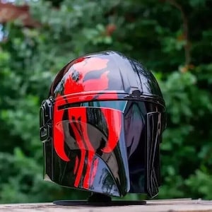 May include: A glossy black helmet with red accents. The helmet features a distinctive design with red markings across the top and face, and a visor. The helmet is likely a costume piece or collectible.