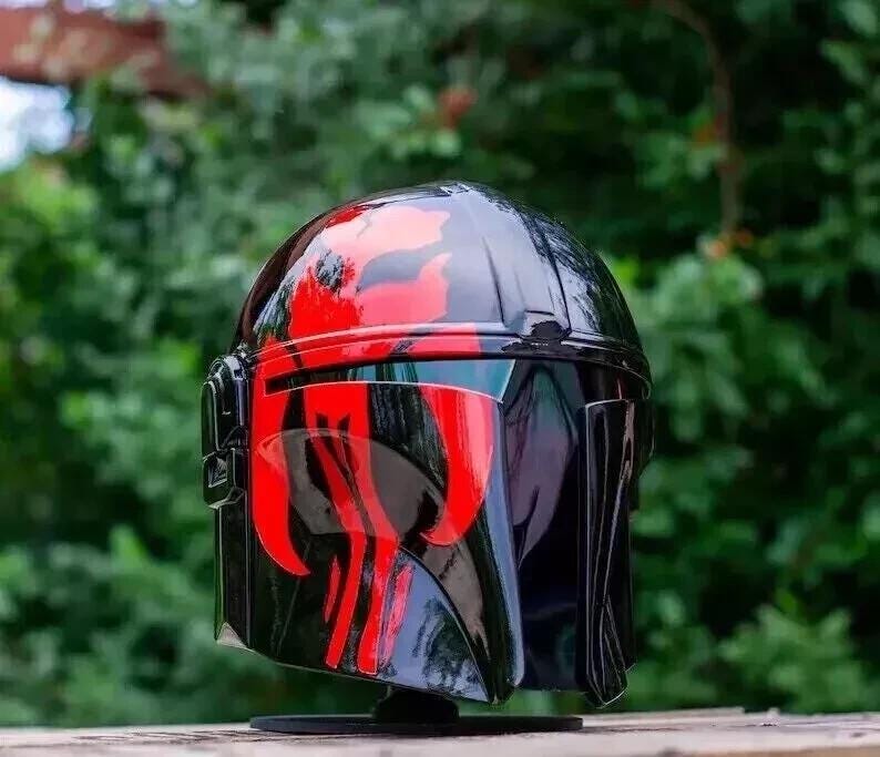 May include: A glossy black helmet with red accents. The helmet features a distinctive design with red markings across the top and face, and a visor. The helmet is likely a costume piece or collectible.