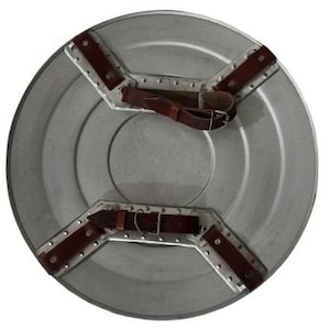 May include: A silver-colored, round shield with brown leather straps and metal accents. The shield has a central circular design and is constructed with riveted metal plates. The straps are secured with buckles.