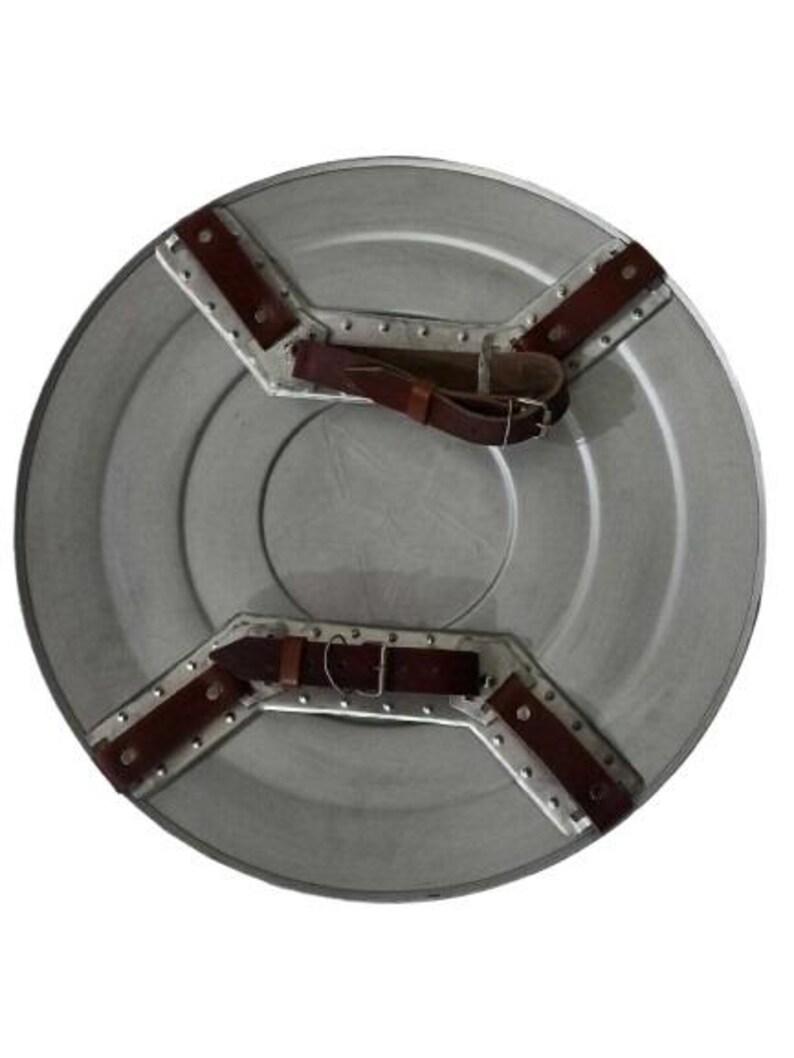 May include: A silver-colored, round shield with brown leather straps and metal accents. The shield has a central circular design and is constructed with riveted metal plates. The straps are secured with buckles.