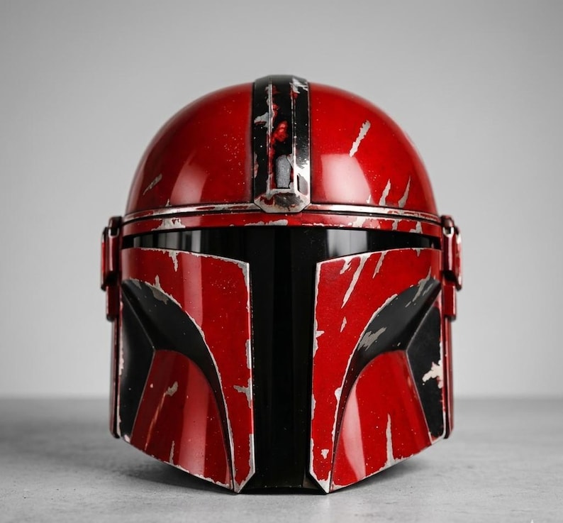 Puede incluir: Un casco mandaloriano rojo y negro con un acabado desgastado. El casco presenta una c&uacute;pula roja brillante y un &aacute;rea de visera negra. Los detalles plateados y desgastados por la batalla se suman al aspecto realista de este art&iacute;culo de colecci&oacute;n.