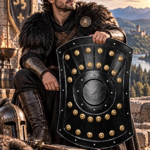 May include: A large, rectangular black shield with rounded corners, featuring a central circular boss and multiple gold-colored sun-shaped studs arranged in rows. The shield has a smooth, dark finish with silver-toned rivets along the edges.