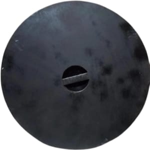 May include: A circular, matte black metal lid featuring a central circular cutout with a horizontal bar spanning across the middle. The surface has a slightly mottled, dark finish with subtle variations in texture across the round plate.