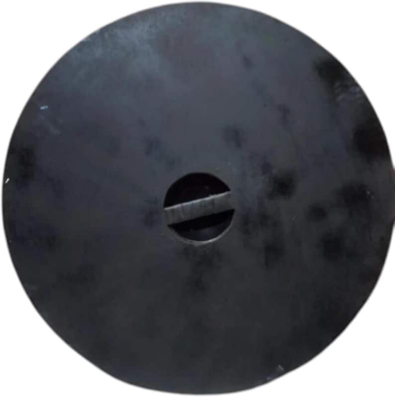 May include: A circular, matte black metal lid featuring a central circular cutout with a horizontal bar spanning across the middle. The surface has a slightly mottled, dark finish with subtle variations in texture across the round plate.