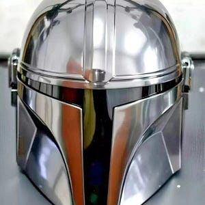 May include: A highly reflective, silver-colored helmet with a distinctive design. The helmet features a rounded top, a visor, and angular cheek plates. The surface is smooth and polished, reflecting the surrounding environment. The overall aesthetic suggests a futuristic or science fiction theme.