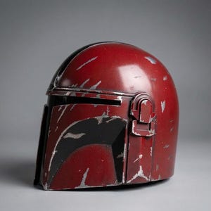 Puede incluir: Un casco rojo desgastado con ara&ntilde;azos plateados y detalles en negro. El casco tiene una visera y un accesorio lateral. El dise&ntilde;o sugiere un tema futurista o de ciencia ficci&oacute;n, posiblemente una pieza de disfraz o de colecci&oacute;n.