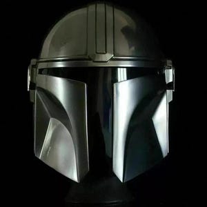 May include: A metallic silver Mandalorian helmet with a dark visor and a sleek, angular design. The helmet has a rounded top and a distinctive T-shaped visor, perfect for cosplay or display.