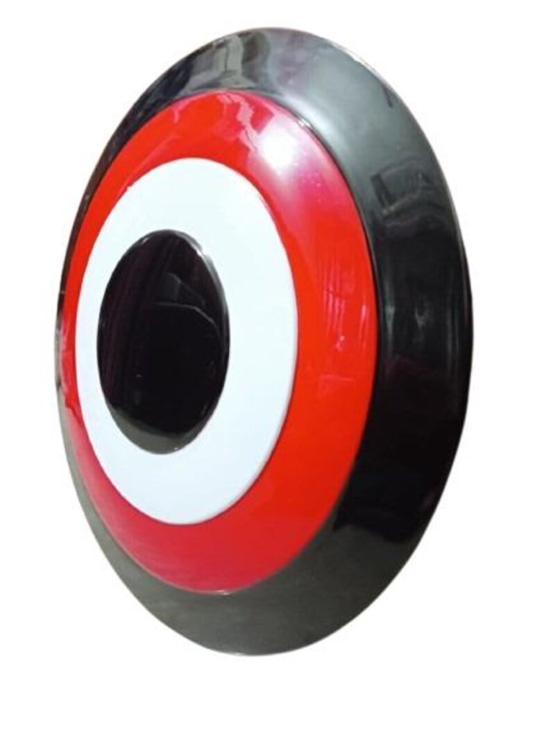 May include: A glossy, circular shield with a black outer rim, a red middle ring, and a white inner ring surrounding a central black circle. The shield has a slightly convex shape.