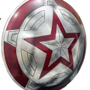 May include: A round, metallic shield with a red and silver color scheme. The shield features a large red star in the center, surrounded by a silver star and a red outer ring. The design is reminiscent of a superhero's shield.