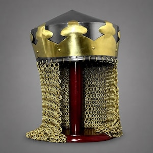 Op de afbeelding: Een stalen helm met een gepolijste donker metalen schedelkap, bekroond met een decoratieve messing band in de vorm van een kroon. Aan de onderrand hangt een lange, goudkleurige maliënkolder van in elkaar grijpende metalen ringen.