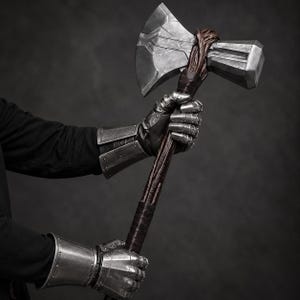 Könnte beinhalten: Eine große Streitaxt mit einem metallisch silbernen Kopf und einem dunkelbraunen, strukturierten Stiel. Die Axt hat eine breite, scharfe Klinge auf der einen Seite und einen blockartigen Hammerkopf auf der anderen, mit braunem Ledergriff.