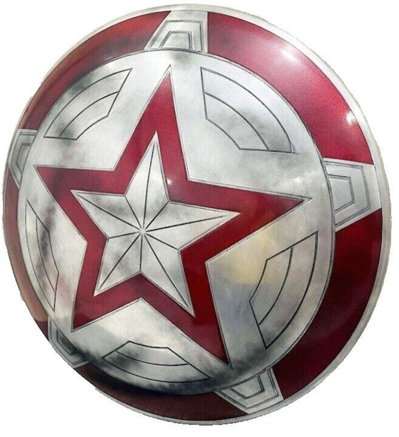 May include: A round, metallic shield with a red and silver color scheme. The shield features a large, red star in the center, surrounded by a silver design. The outer rim is also red, with silver accents. The shield has a weathered appearance.