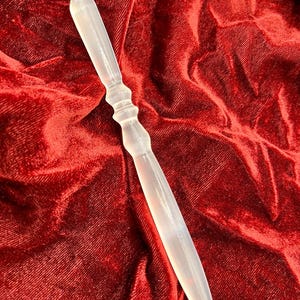 Op de afbeelding: Een doorschijnende, melkwitte glazen toverstaf of briefopener met een puntig uiteinde en een taps toelopende, ronde handgreep met drie duidelijke ribbels. Het object heeft een glad, gepolijst oppervlak en een slanke, langwerpige vorm die uitloopt in een punt.