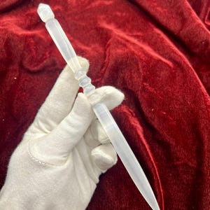 Op de afbeelding: Een doorschijnende witte briefopener met een glad, taps toelopend blad en een decoratief, geribbeld handvat. Het object heeft een puntig uiteinde en een gefacetteerde, kristalachtige bovenkant, met een semi-transparante uitstraling.