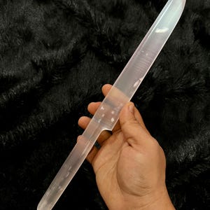 Puede incluir: Un cuchillo translúcido y transparente con una hoja lisa y alargada y un mango redondeado. El objeto está fabricado con un material sólido similar al vidrio, con una punta afilada y un borde recto que se estrecha hacia la sección del mango.