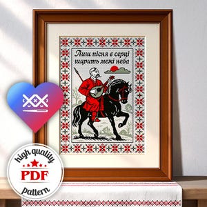 May include: Framed cross-stitch art featuring a man in red attire playing a stringed instrument while riding a black horse. The artwork includes text and floral border designs in red, white, and black.