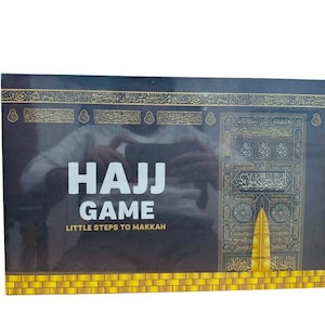 Könnte beinhalten: Ein Brettspiel mit dem Titel "Hajj Game: Little Steps to Makkah". Die Spielbox ist überwiegend schwarz mit goldenen Akzenten und zeigt eine Illustration der Kaaba. Der Text ist in Weiß und Gold gehalten.