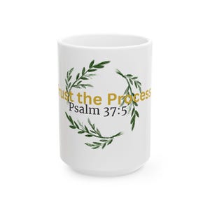 May include: White ceramic mug with the text "Trust the Process" in gold lettering, and "Psalm 37:5" in black. The text is surrounded by a green leafy wreath design.