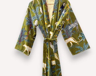 May include: Olive green velvet robe with a jungle-themed print featuring leopards, zebras, toucans, and palm trees. The robe has long sleeves and a matching belt. The interior lining has a striped pattern. The robe is hanging on a wooden hanger.