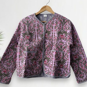 Op de afbeelding: Gewatteerde jas met bloemenpatroon in roze, groene en rode tinten. De jas heeft een ronde kraag, twee zakken en een gestreepte voering. Op een houten hanger.