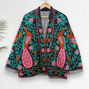 May include: A black embroidered jacket with a peacock design. The jacket features brown, pink, and green peacock figures and floral patterns. The jacket has a striped lining and trim, and is hanging on a wooden hanger.