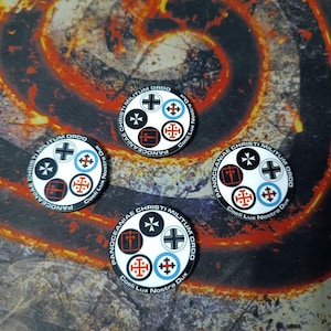 May include: Four white, circular tokens with various cross designs in black, red, and blue. Each token has the text "Panoceaniae Christi Militum Ordo" and "Coeli Lux Nostra Dux" around the edge. The background is a dark, textured surface.