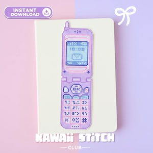 Op de afbeelding: Kruissteekpatroon van een retro klaptelefoon in paarse en blauwe tinten, met de tijd 10:00 weergegeven op het scherm. De telefoon ligt op een crèmekleurig oppervlak, met de tekst "KAWAII STITCH CLUB" eronder.