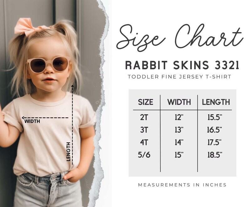 May include: A child in a light-colored t-shirt and sunglasses. The image features a size chart for Rabbit Skins 3321 toddler fine jersey t-shirts, with measurements in inches. The chart shows sizes 2T to 5/6, with widths from 30.5cm to 38.1cm and lengths from 39.4cm to 47cm.